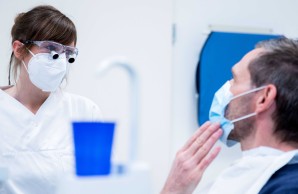 Dr. Josefine Holtermann im Patientengespräch, beide tragen einen Mund-Nasen-Schutz. Der Patient passt sich an den linken Unterkiefer