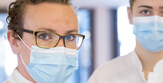 Einen Porträtaufnahme. Dr. Louise Roggelin blickt den Betrachter sehr intensiv an. Sie trägt einen hellblauen Mund-Nasen-Schutz