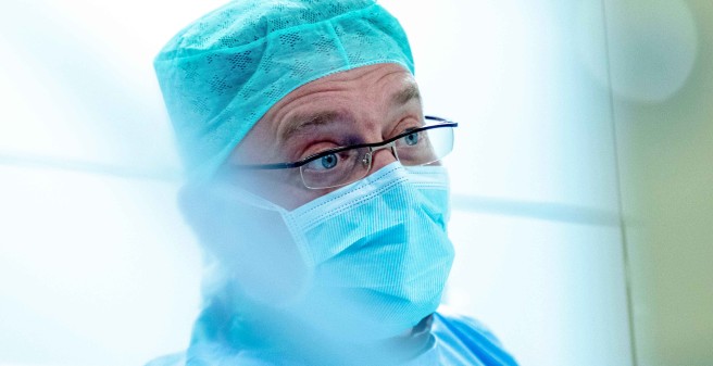 Dr. Marc Remmel blickt konzentriert, ein Porträt. Remmel trägt türkisfarbenen Mund-Nasen-Schutz und Kappe