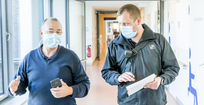 Waldemar Ringe und Ricardo Zbierski gehen nebeneinander durch einen Klinikgang, sie tragen Mund-/Nasenschutz Masken